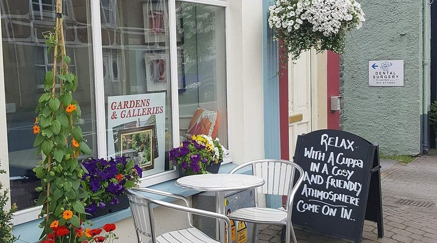 The café's front door with a chalkboard outside reading Relax with a cuppa in a cosy and friendly atmosphere, come on in, with a small table and two chairs