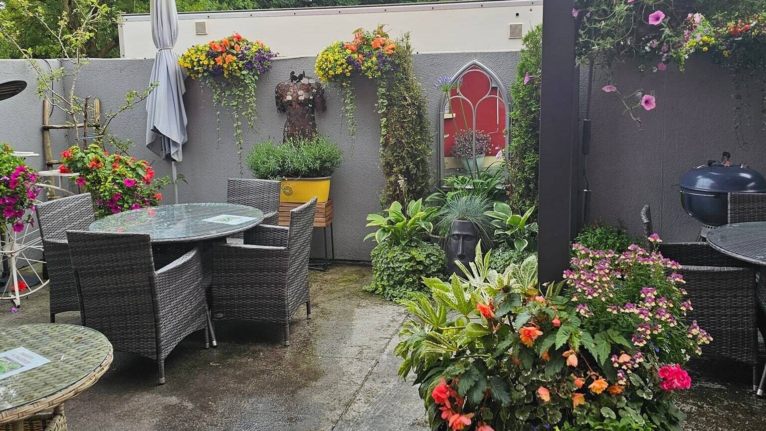 The covered courtyard at The Found Out Cafe with wicker tables, a red awning and flower baskets on a grey wall