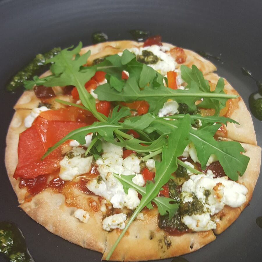 A flatbread topped with rocket, red peppers and white cheese on a black plate